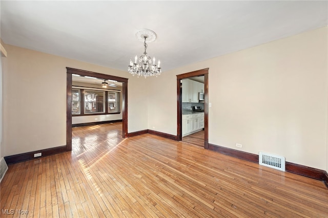 empty room with light wood-type flooring, baseboards, visible vents, and a notable chandelier