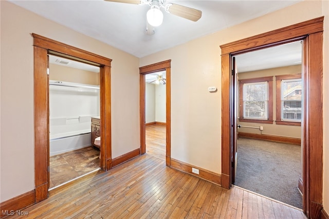 corridor with light wood-style floors, visible vents, and baseboards