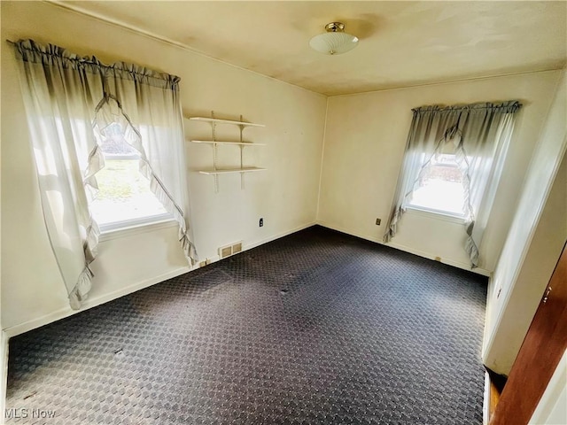 unfurnished room featuring a wealth of natural light, visible vents, and baseboards