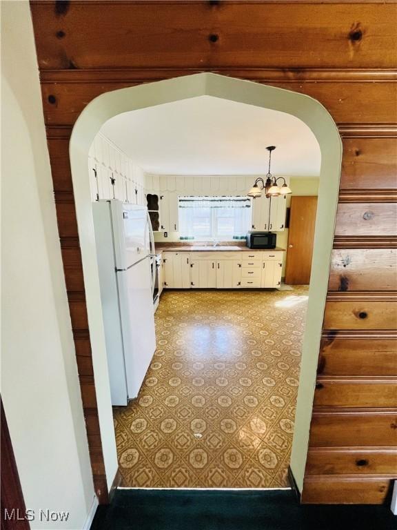 kitchen with arched walkways, freestanding refrigerator, white cabinetry, black microwave, and pendant lighting