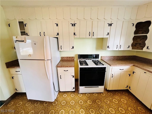 kitchen featuring dark countertops, range with gas cooktop, white cabinetry, and freestanding refrigerator