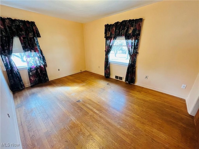 empty room featuring wood finished floors, visible vents, and baseboards