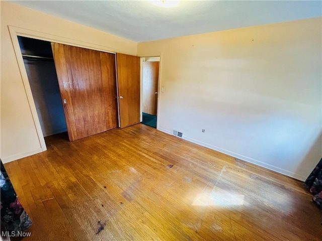 unfurnished bedroom with hardwood / wood-style floors, a closet, visible vents, and baseboards