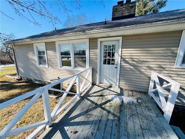 view of exterior entry featuring roof with shingles, a chimney, a wooden deck, and central AC unit
