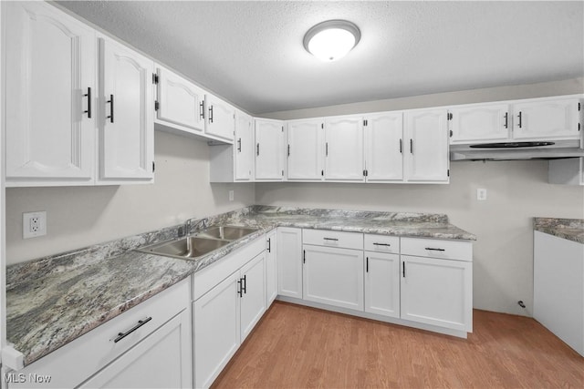 kitchen with white cabinets, under cabinet range hood, a textured ceiling, light wood-style floors, and a sink