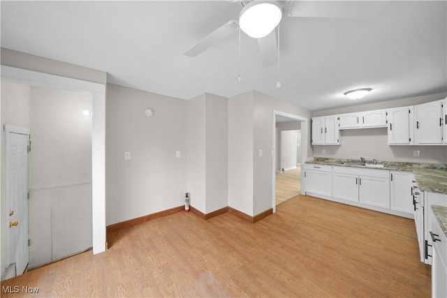 kitchen with white cabinets, a sink, light wood-style flooring, and light stone countertops