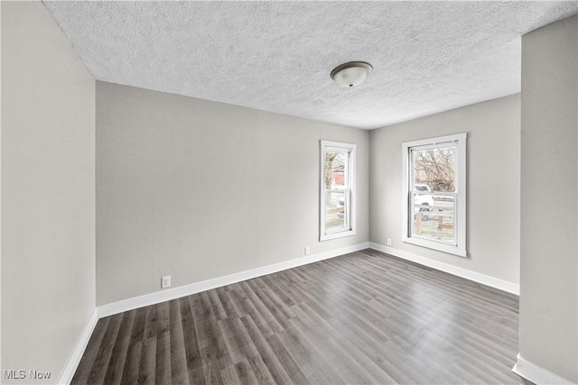 empty room with dark wood-style floors, a textured ceiling, and baseboards