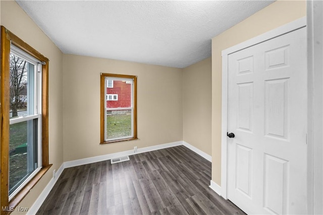 empty room featuring dark wood-style floors, visible vents, a textured ceiling, and baseboards