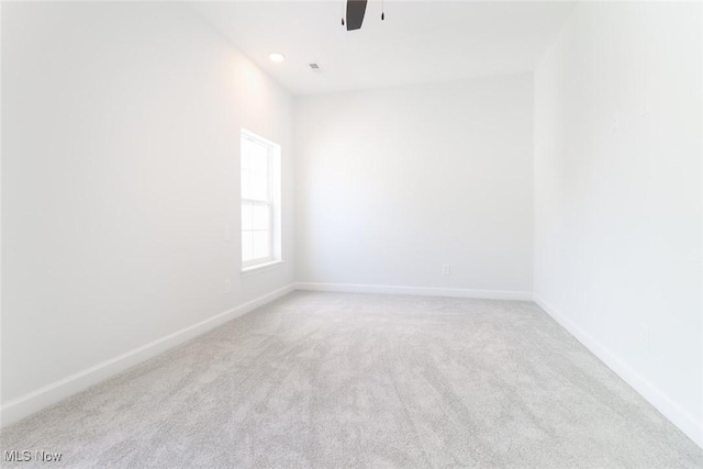 spare room featuring light carpet, ceiling fan, and baseboards