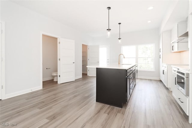 kitchen with a sink, stainless steel oven, light countertops, a center island with sink, and pendant lighting