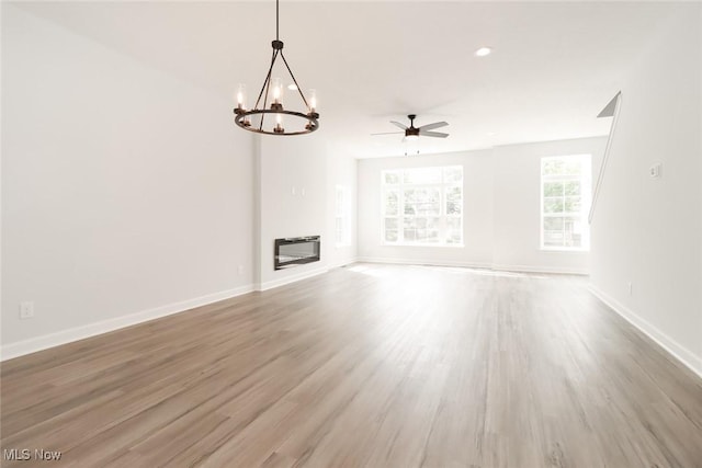 unfurnished living room with heating unit, a glass covered fireplace, wood finished floors, baseboards, and ceiling fan with notable chandelier