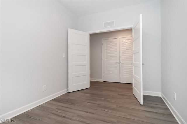 unfurnished bedroom featuring baseboards, a closet, visible vents, and wood finished floors