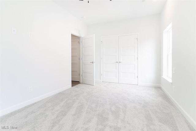 unfurnished bedroom featuring light carpet, ceiling fan, baseboards, and a closet