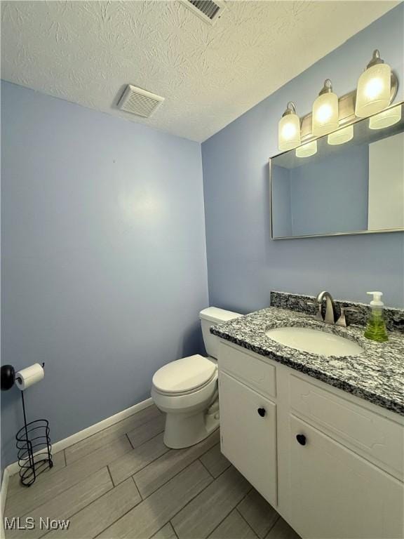 half bath with visible vents, toilet, vanity, a textured ceiling, and baseboards