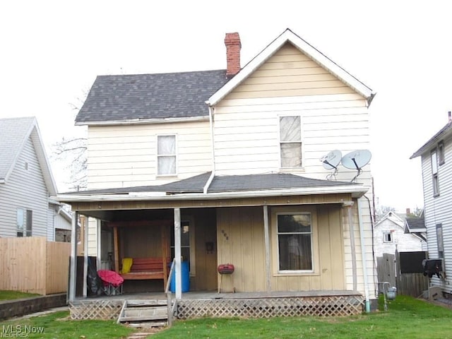 back of house with a yard, a chimney, a shingled roof, covered porch, and fence