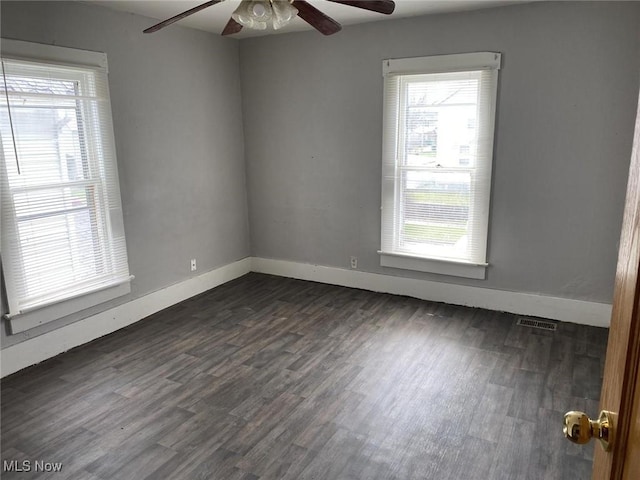 unfurnished room featuring baseboards, visible vents, and dark wood finished floors