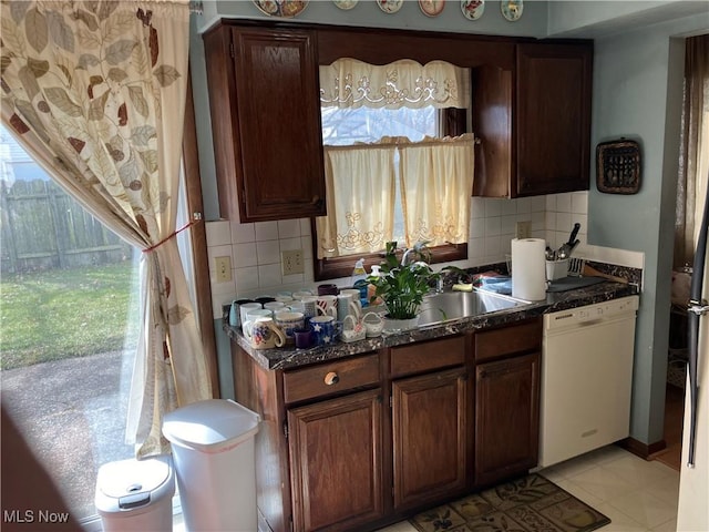 kitchen with a sink, tasteful backsplash, dark stone countertops, and dishwasher