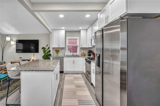 kitchen featuring white cabinets, appliances with stainless steel finishes, open floor plan, a kitchen breakfast bar, and backsplash