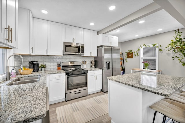 kitchen featuring a breakfast bar, stainless steel appliances, white cabinetry, a sink, and a kitchen island