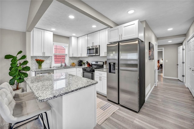 kitchen featuring appliances with stainless steel finishes, light wood-style flooring, a sink, and white cabinetry