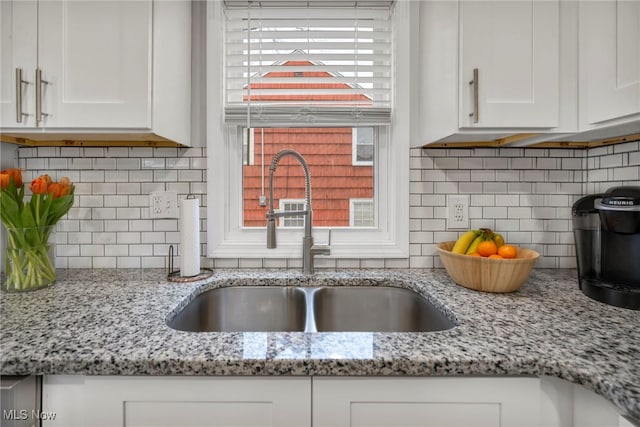 kitchen featuring a healthy amount of sunlight, a sink, light stone countertops, and white cabinets