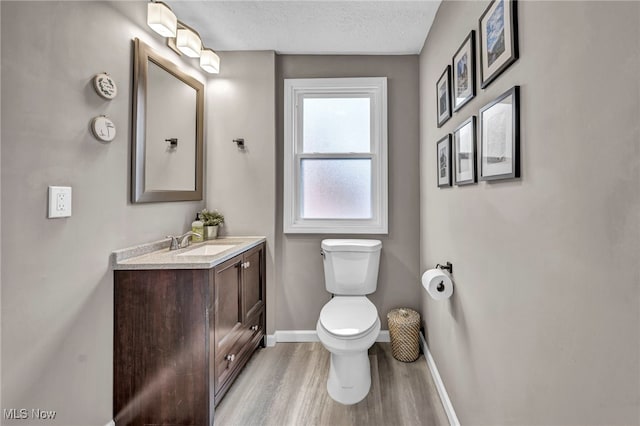 half bathroom with a textured ceiling, toilet, wood finished floors, vanity, and baseboards