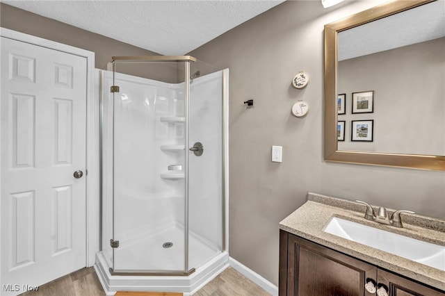 bathroom with a textured ceiling, a stall shower, wood finished floors, and vanity