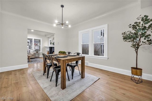 dining space with light wood finished floors, baseboards, a fireplace, and ornamental molding