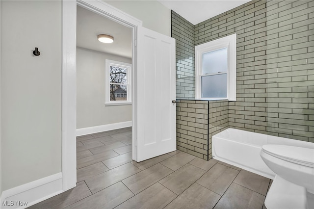 bathroom with toilet, a washtub, and baseboards