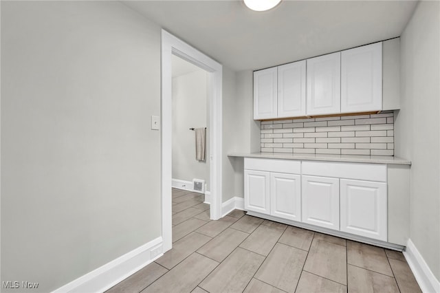 interior space featuring baseboards, white cabinetry, light countertops, and decorative backsplash