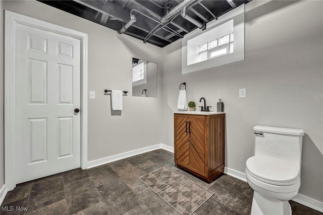 bathroom featuring stone finish floor, vanity, toilet, and baseboards