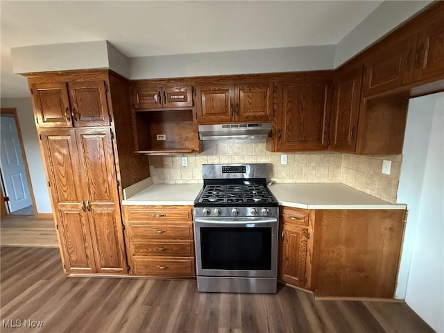 kitchen featuring under cabinet range hood, light countertops, backsplash, stainless steel range with gas cooktop, and dark wood-style floors