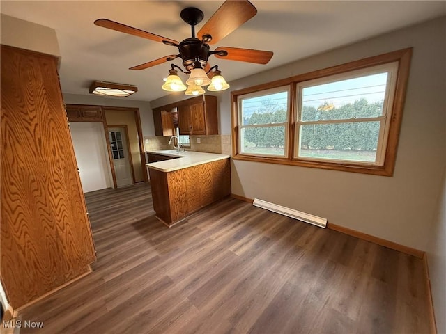 kitchen featuring brown cabinetry, dark wood-type flooring, a peninsula, light countertops, and a sink