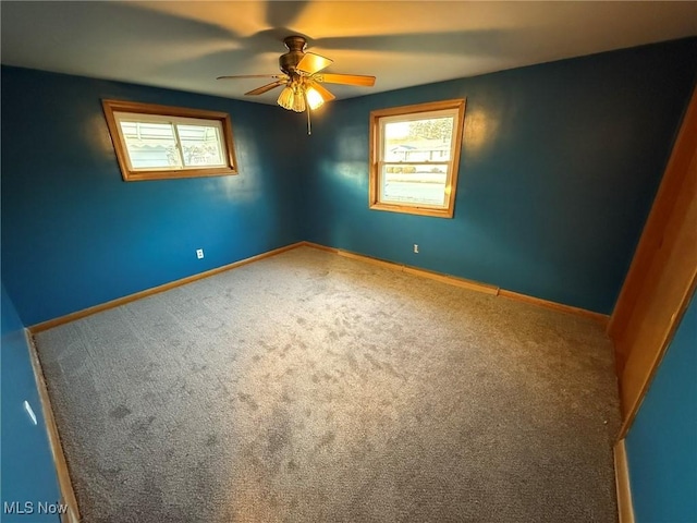 carpeted empty room with a ceiling fan, a wealth of natural light, and baseboards