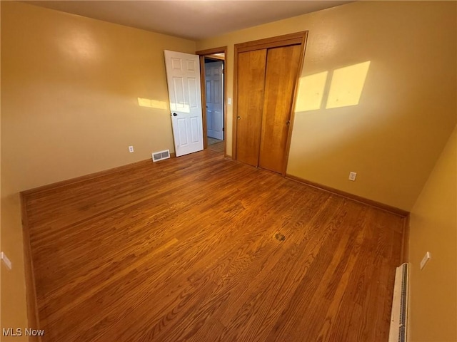 unfurnished bedroom with baseboards, a closet, visible vents, and wood finished floors