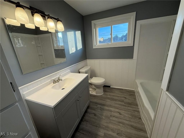 bathroom featuring toilet, a wainscoted wall, wood finished floors, vanity, and a bathtub