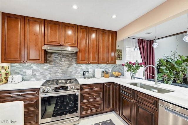 kitchen featuring tasteful backsplash, light countertops, appliances with stainless steel finishes, a sink, and under cabinet range hood