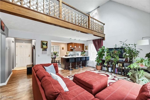 living area with a high ceiling, light wood-type flooring, and baseboards