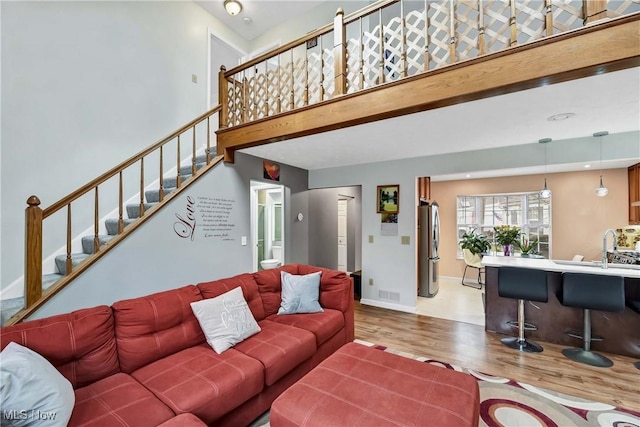 living area featuring baseboards, a high ceiling, stairway, and light wood-style floors