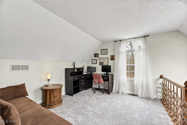 home office featuring a textured ceiling, light carpet, visible vents, baseboards, and vaulted ceiling