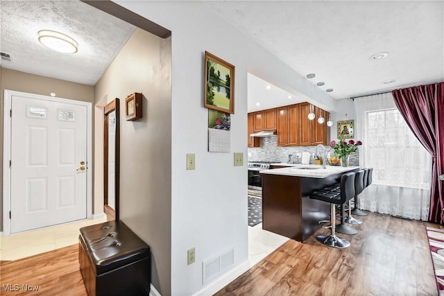 kitchen featuring a sink, visible vents, brown cabinets, tasteful backsplash, and a kitchen bar