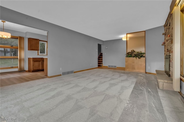 unfurnished living room with stairway, a fireplace, visible vents, and light colored carpet