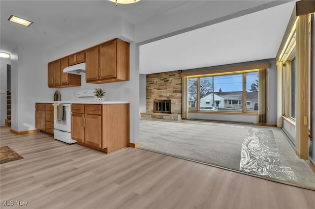 kitchen with white electric stove, light countertops, light wood-style floors, a stone fireplace, and under cabinet range hood