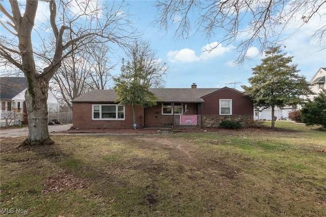 ranch-style house featuring brick siding, a chimney, a porch, fence, and a front lawn