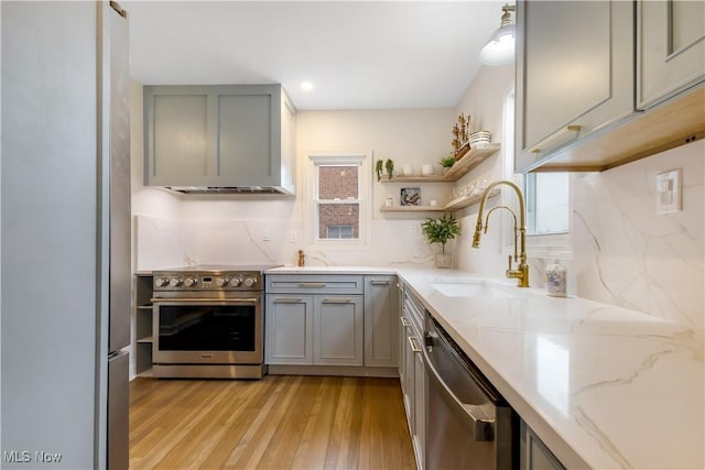 kitchen featuring light stone counters, stainless steel appliances, a sink, light wood-type flooring, and gray cabinets