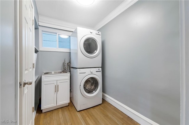 clothes washing area with light wood-style flooring, a sink, cabinet space, stacked washer and clothes dryer, and crown molding