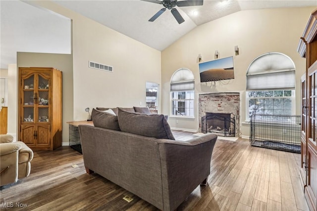 living room featuring high vaulted ceiling, a fireplace, visible vents, and wood finished floors