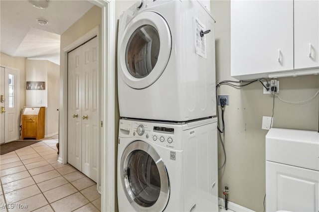 clothes washing area featuring stacked washing maching and dryer, light tile patterned floors, and laundry area