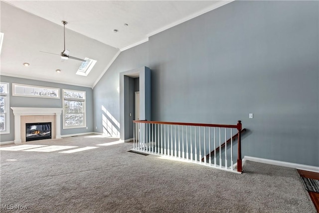 unfurnished living room with ornamental molding, lofted ceiling with skylight, carpet, and baseboards