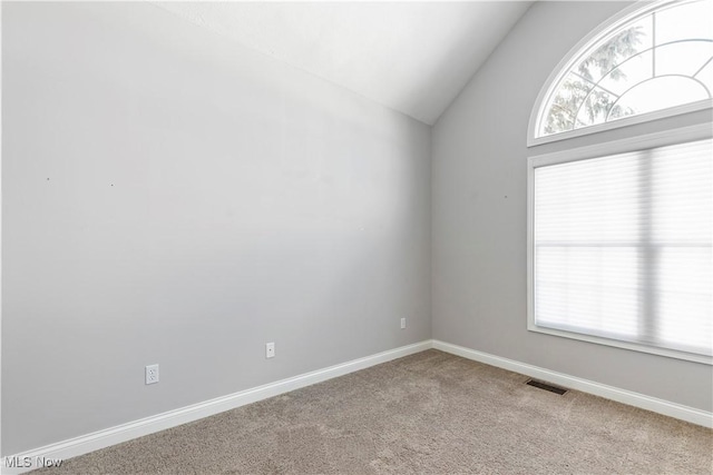 spare room featuring lofted ceiling, carpet flooring, plenty of natural light, and visible vents